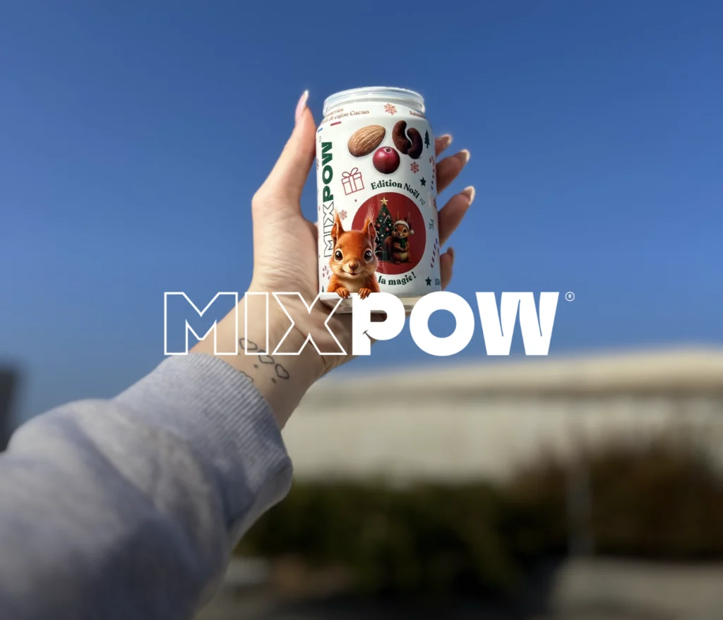 Canette Mixpow édition Noël tenue par une main, avec des amandes, noix de cajou et cacahuètes, sur fond de ciel bleu. Collations saines et recyclable.